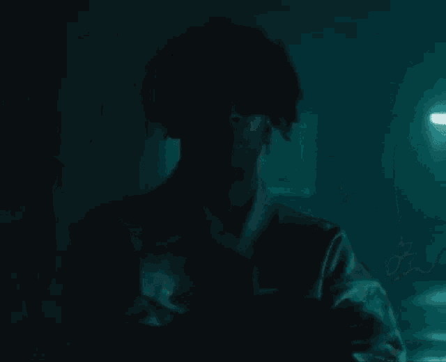 a man in a suit and tie is standing in a dark room with a blue light behind him .