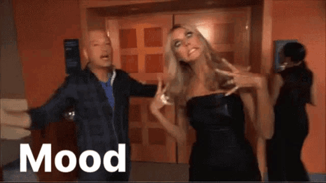 a woman in a black dress is standing next to a man in a blue shirt and the word mood is on the bottom