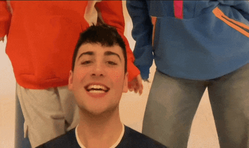 a young man in a blue shirt is smiling in front of two other people