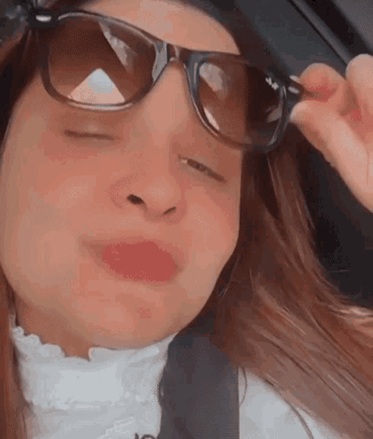 a woman wearing sunglasses is sitting in a car with her eyes closed and making a funny face .
