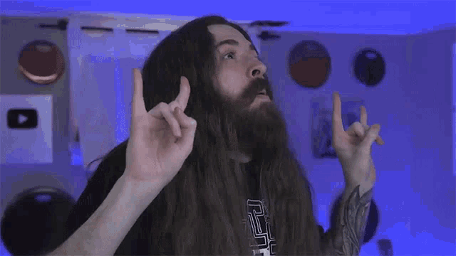 a man with long hair and a beard making a devil horns sign