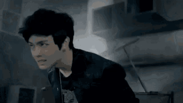 a young man in a black jacket is standing in a dark room looking at the camera .