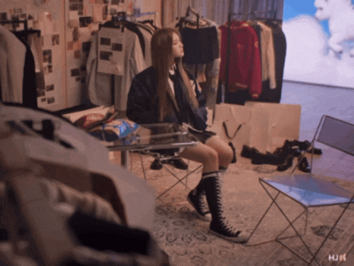 a woman sits on a chair in a room with clothes hanging on a rack and the word hui on the bottom right