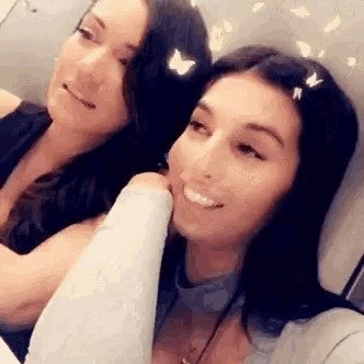 two women are sitting next to each other on an airplane and smiling .