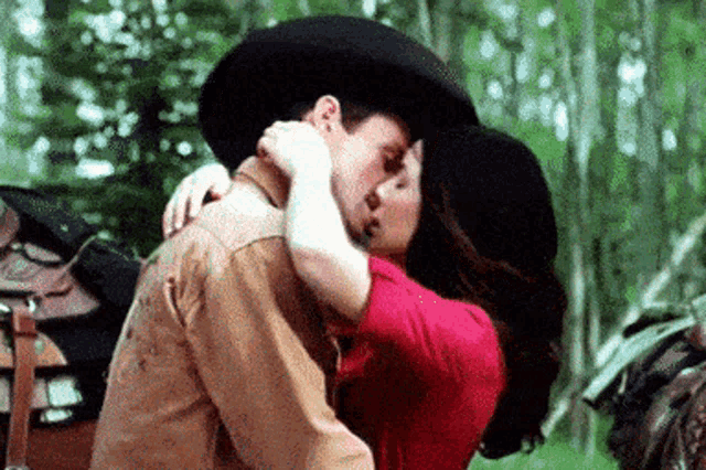 a man in a cowboy hat and a woman in a red shirt are kissing .