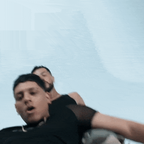 a couple of men are standing next to each other and one of them is laying on the other 's back .