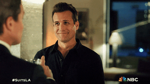 a man in a black shirt is smiling while talking to another man in a suit with the nbc logo in the background