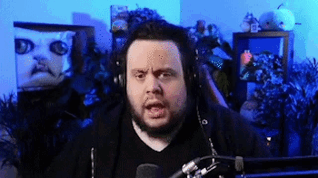 a man with a beard is wearing headphones and talking into a microphone in front of a cat .