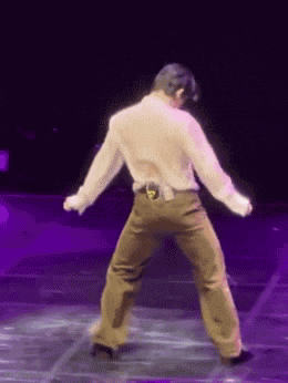 a man in a white shirt and brown pants is dancing on a stage in front of a purple light .