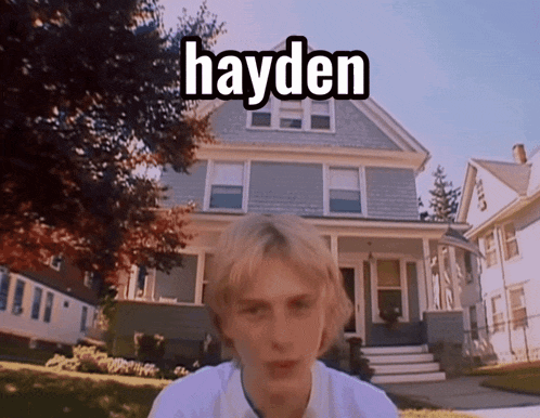 a young man stands in front of a house with the name hayden on it