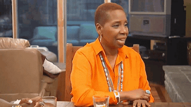 a woman in an orange shirt is sitting at a table with a glass of water and a pen .