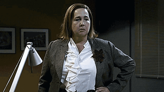 a woman wearing a white ruffled blouse and a brown jacket