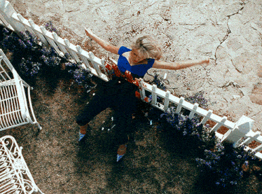 a woman in a blue top and black pants is standing next to a white fence