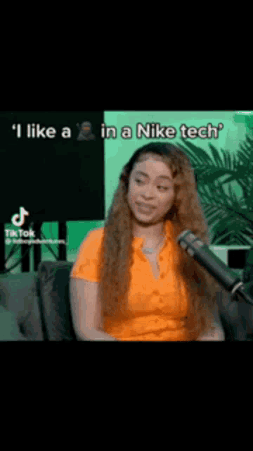 a woman in an orange shirt is sitting in front of a microphone and says i like a in a nike tech