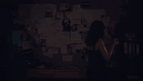 a woman stands in front of a bulletin board with papers on it including one that says never explain