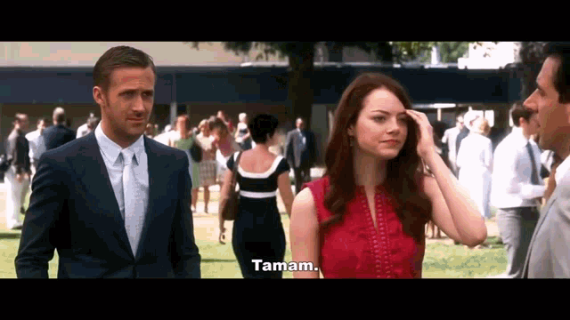 a man in a suit and tie is standing next to a woman in a red dress who says tamam
