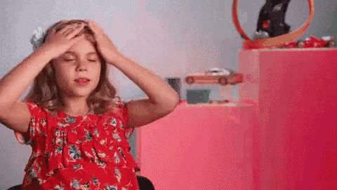 a little girl is holding her head while sitting in front of a hot wheels track .