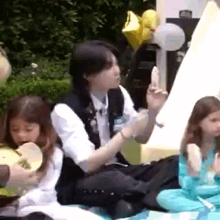 a group of people are sitting on a blanket in a park eating food .
