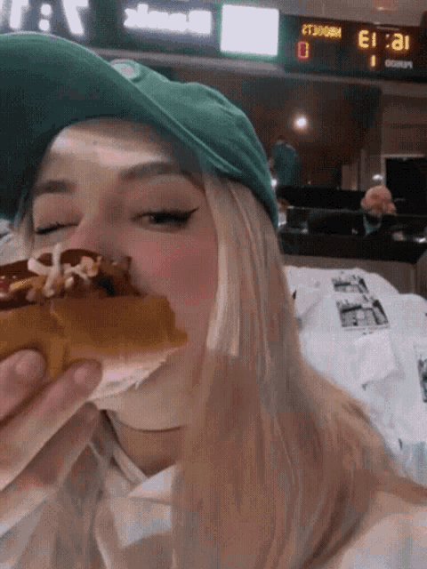 a woman in a green hat eating a hot dog