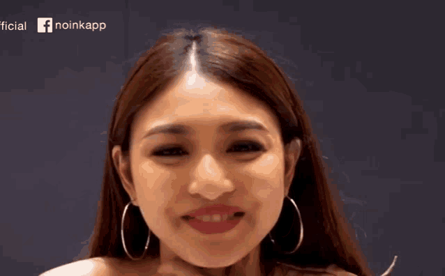 a woman wearing hoop earrings is smiling for the camera with a facebook logo in the background