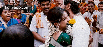 a bride and groom kissing in front of a crowd of people with the website kulfyapp.com in the corner