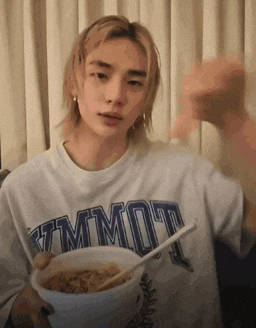 a young man wearing a shirt that says tmmot is holding a bowl of food with a spoon