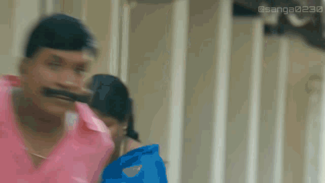 a man in a pink shirt is holding a knife in his mouth while standing next to a woman in a blue dress .