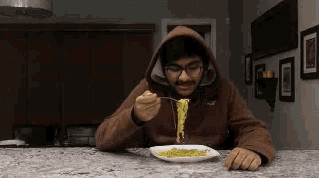 a man in a hooded jacket is eating noodles with a fork from a plate .