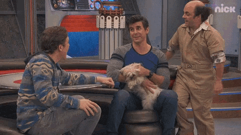 three men and a dog are sitting in front of a sign that says nick on it
