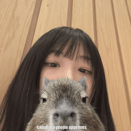 a girl is holding a capybara in front of her face
