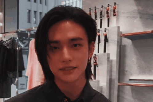 a young man with long hair is standing in front of a clothes rack .