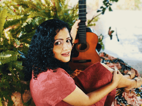 a woman in a red dress holds a guitar in her lap