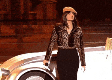 a woman in a leopard print jacket is holding a microphone in front of a car