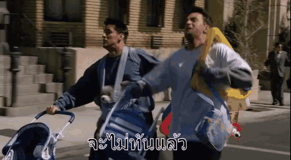 two men are pushing a stroller down a street and one of them is carrying a baby