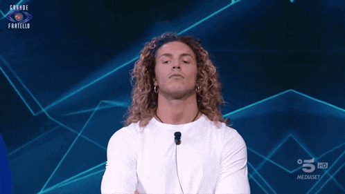 a man with long curly hair stands in front of a blue background that says grande fratello on it