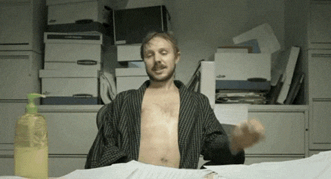 a man without a shirt is sitting at a desk in front of a stack of boxes and a bottle of hand sanitizer