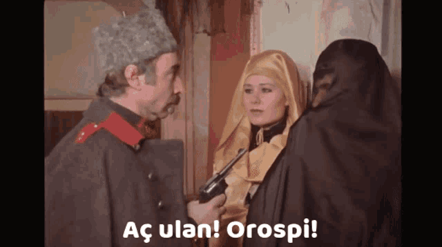 a man in a military uniform holds a gun in front of two women and says " ac ulan orospi " at the bottom