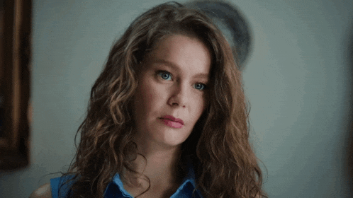 a woman with curly hair and blue eyes is looking at the camera