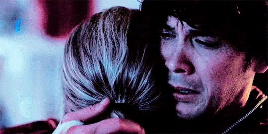 a man and a woman are hugging each other in a dark room and the man is crying .