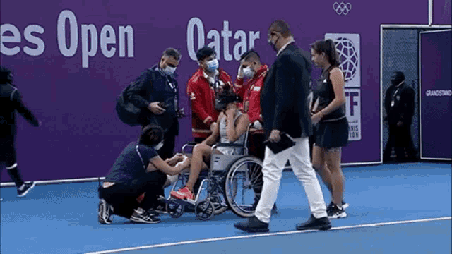 a woman in a wheelchair is being helped on a tennis court by a group of people .