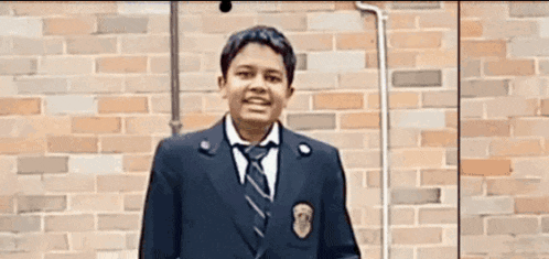 a young boy in a suit and tie stands in front of a brick wall