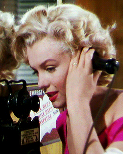a woman in a pink dress is talking on an old fashioned phone