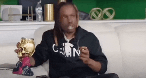 a man with dreadlocks is sitting on a couch holding a skull and a cigarette .