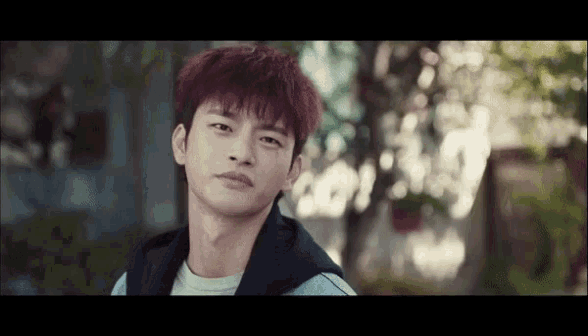 a young man with red hair is standing in front of a tree and looking at the camera .