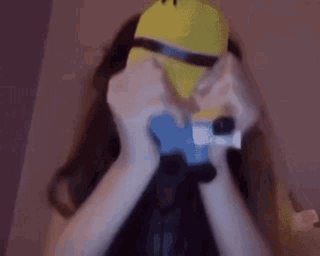 a woman wearing a yellow minion mask is holding a blue object in front of her face