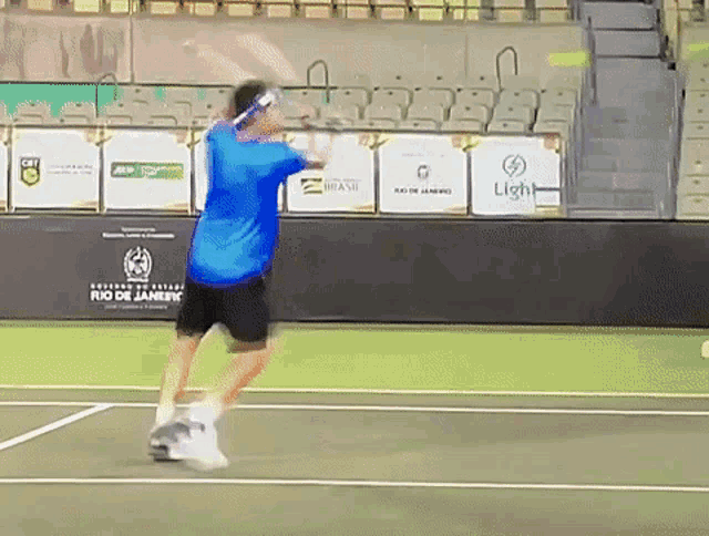 a man in a blue shirt is swinging a tennis racket on a tennis court sponsored by light and brasil