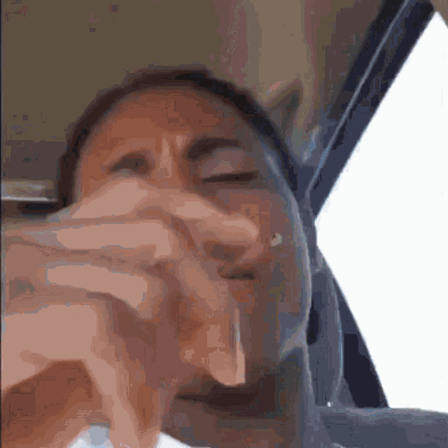 a woman is sitting in a car with her eyes closed and her hands on her face .