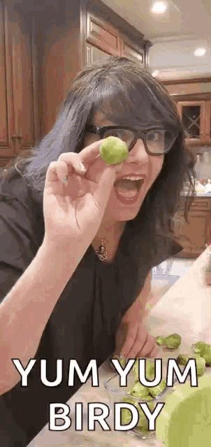 a woman wearing glasses is holding a lime in her hand and eating it .