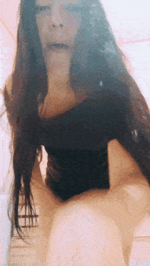 a woman with long hair and a black top is sitting on a bed