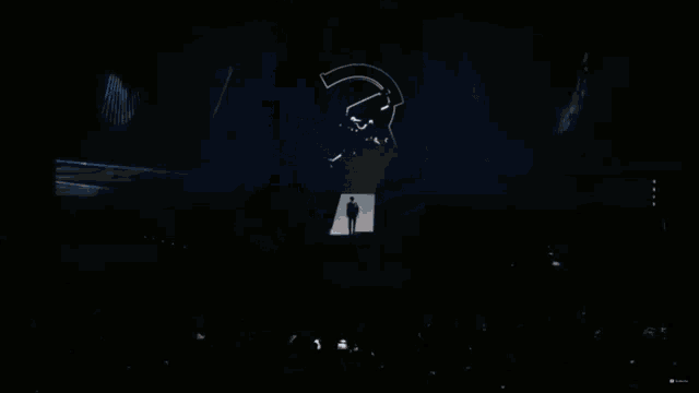 a man stands on a stage in front of a large screen that has a skull on it